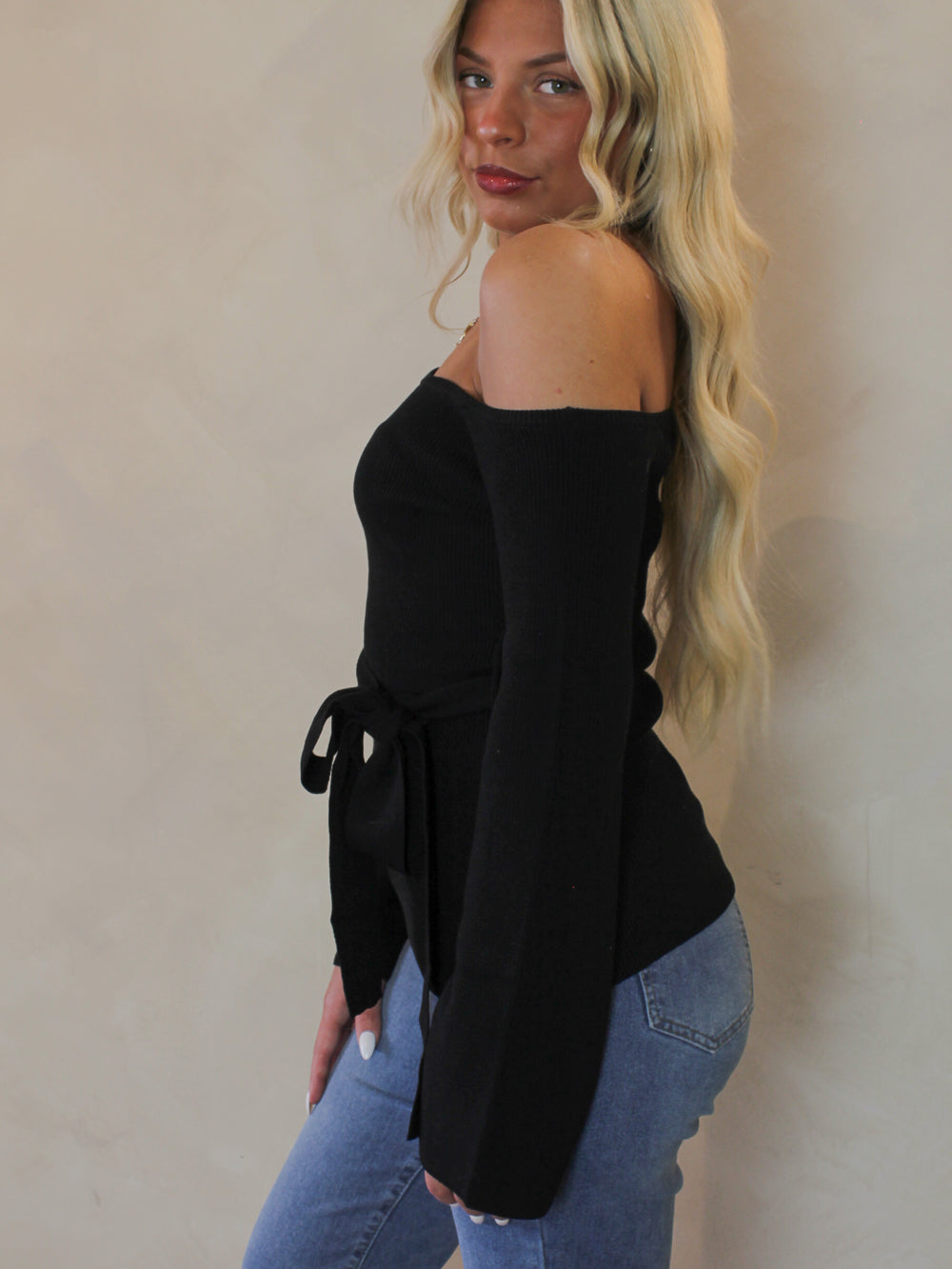 Woman wearing a black off the shoulder sweater with flared sleeves 