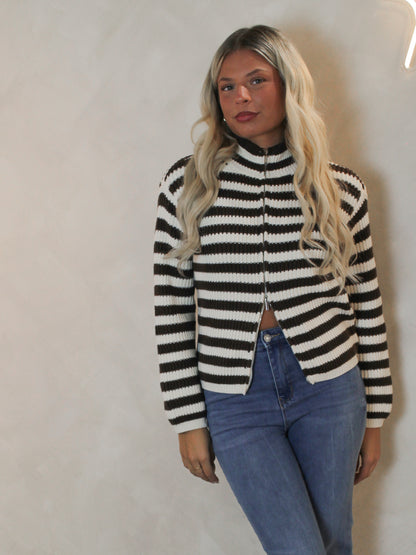 Woman wearing a mock neck cardigan with a brown and cream stripe pattern and zip up detail.
