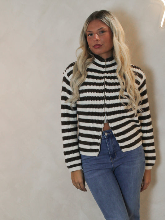 Woman wearing a mock neck cardigan with a brown and cream stripe pattern and zip up detail.