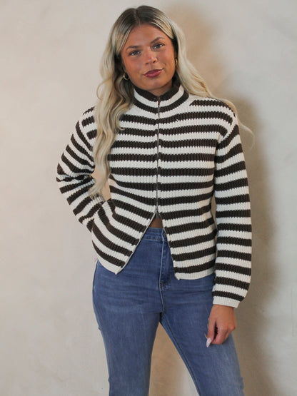A woman with blonde hair wearing a black and white horizontally striped zip-up knit sweater styled with blue jeans.