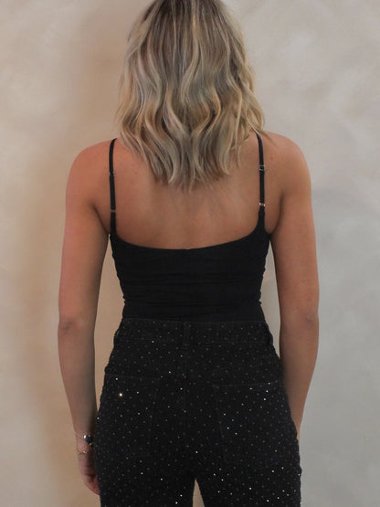 Woman wearing a black cami bodysuit with rhinestone denim pants