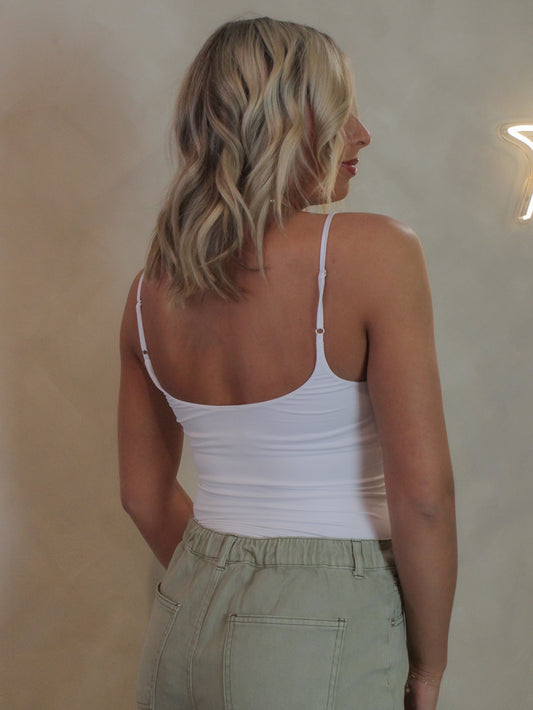 Woman wearing a white cami bodysuit with adjustable straps and sage green pants