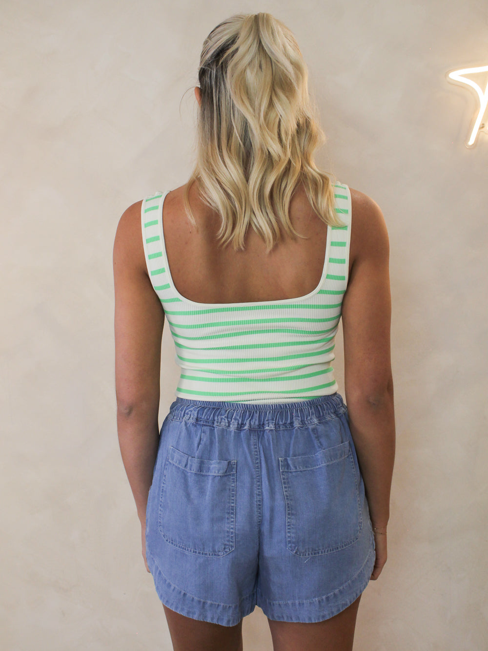 Model wearing a green and white stripe bodysuit with denim shorts