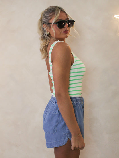 Model showing the side view of a green and white stripe bodysuit styled with denim shorts and sunglasses