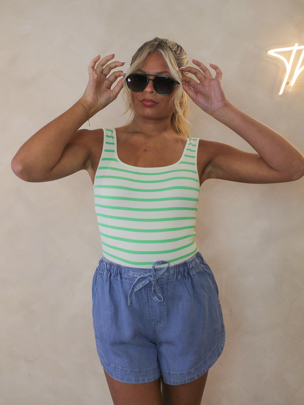 Woman wearing a green and white striped bodysuit styled with blue tencel shorts and sunglasses for summer