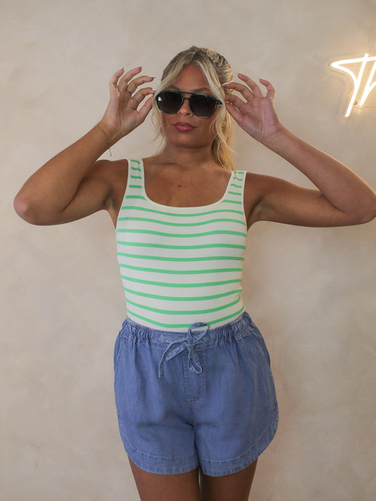 Woman wearing a green and white striped bodysuit styled with blue tencel shorts and sunglasses for summer