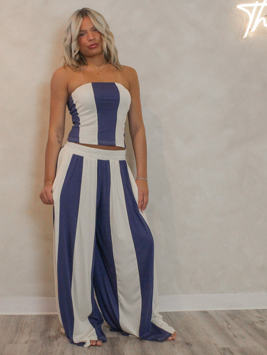 Woman wearing a blue and cream striped summer set with a strapless top and wide leg pants.