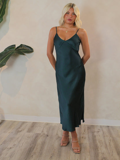 Woman wearing a simple satin midi dress in a dark emerald color 