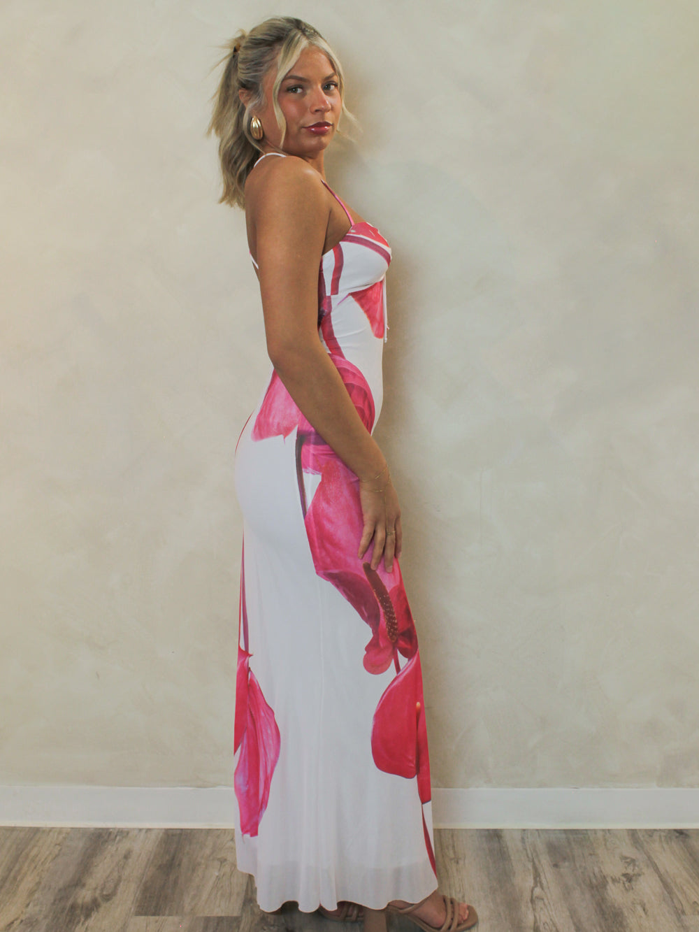 Girl wearing a fitted, white, mesh maxi dress with large floral print design paired with gold earrings for a summer vacation