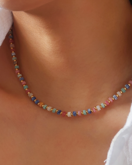 A close-up of a person woman wearing a  delicate beaded necklace with small multicolored round beads and gold spacer accents.