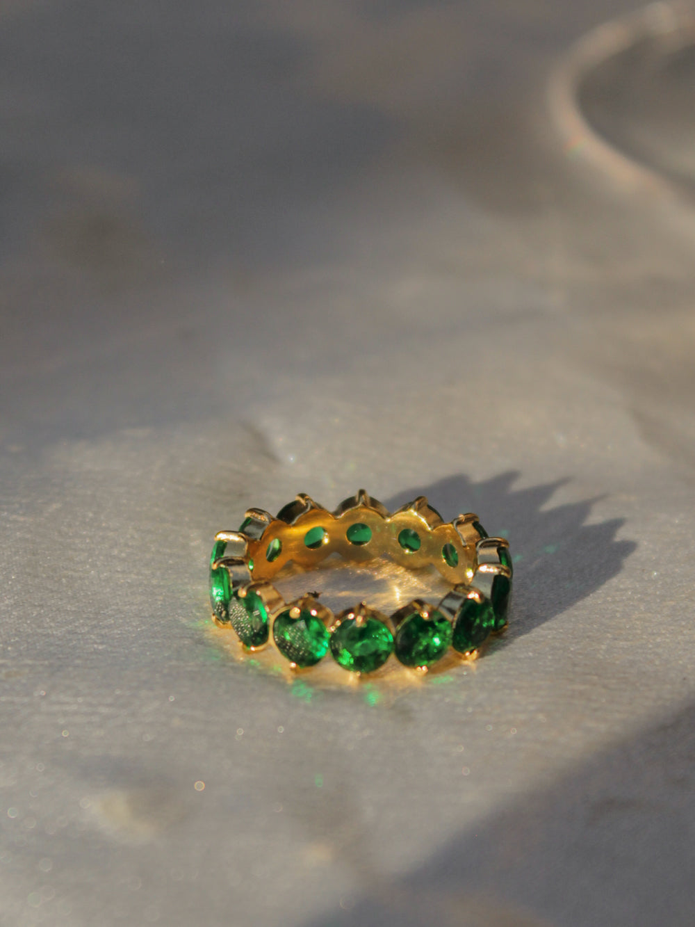 A gold eternity ring set with round emerald green gemstones