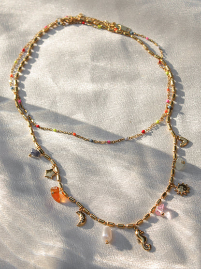 a double layered gold necklace with a colorful beaded layer and a layer with ocean and celestial charms