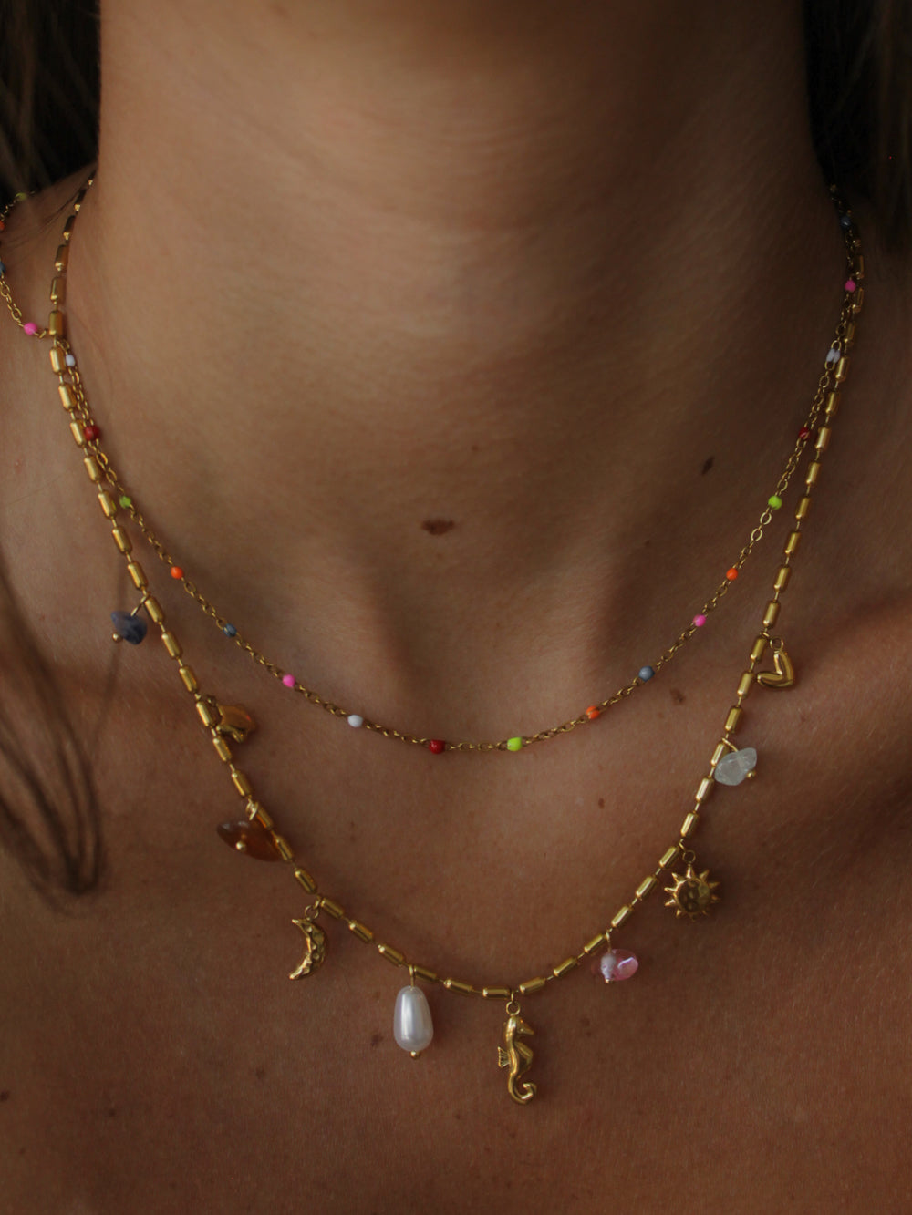 a close up of a girl wearing a double layered gold necklace with sea creature and celestial charms