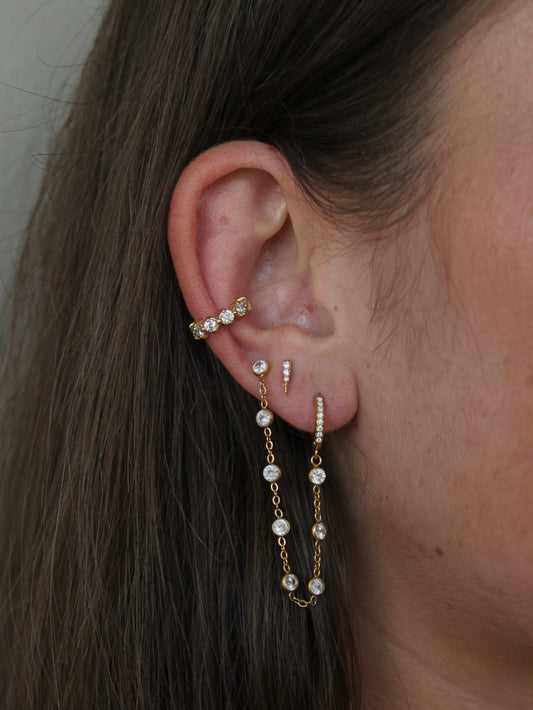 woman wearing a gold earring stack featuring a gold and bezel set ear cuff