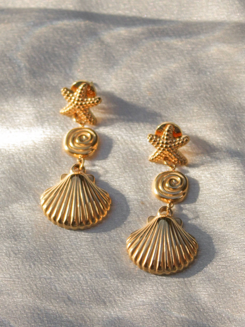 a pair of gold shell drop earrings, featuring a starfish and clam shell