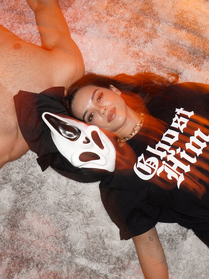 Halloween aesthetic picture with a woman wearing a "Ghost Him" Tee laying next to a person wearing a ghost face mask