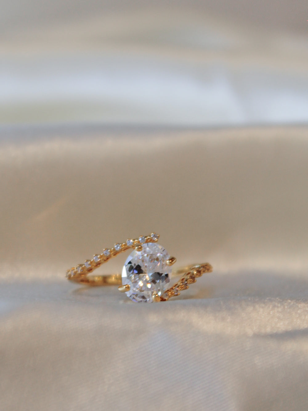 A gold ring with a large oval clear center stone and a twisted band accented with small clear stone.