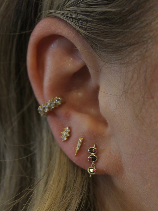 A close-up of a person's ear showcasing multiple gold stud earrings featuring a olive studs.