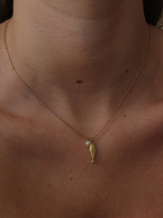 Dainty gold necklace with a fish and pearl charms on a model