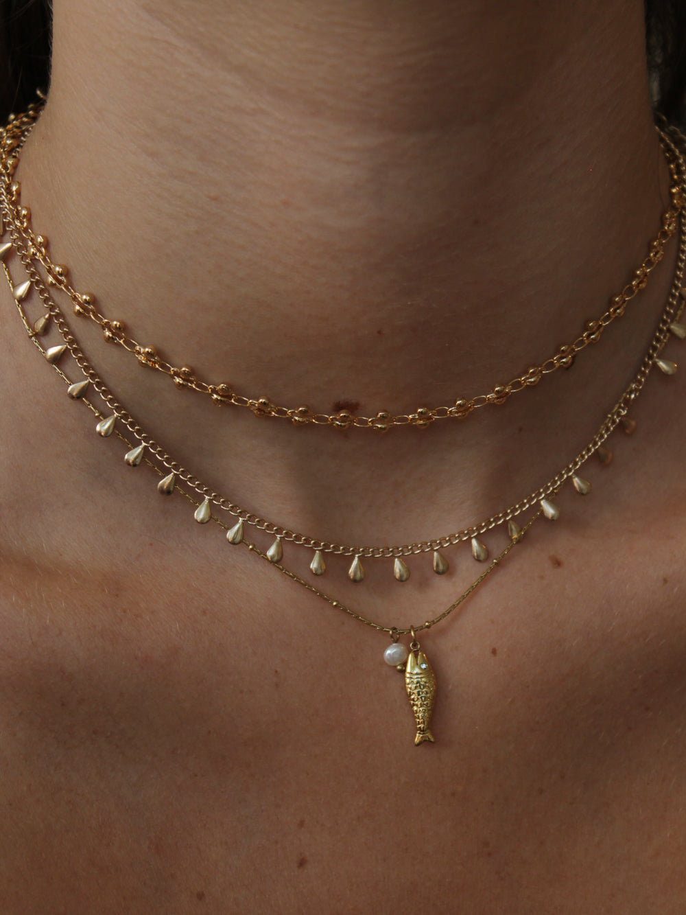Gold necklace stack featuring a fish pendant necklace