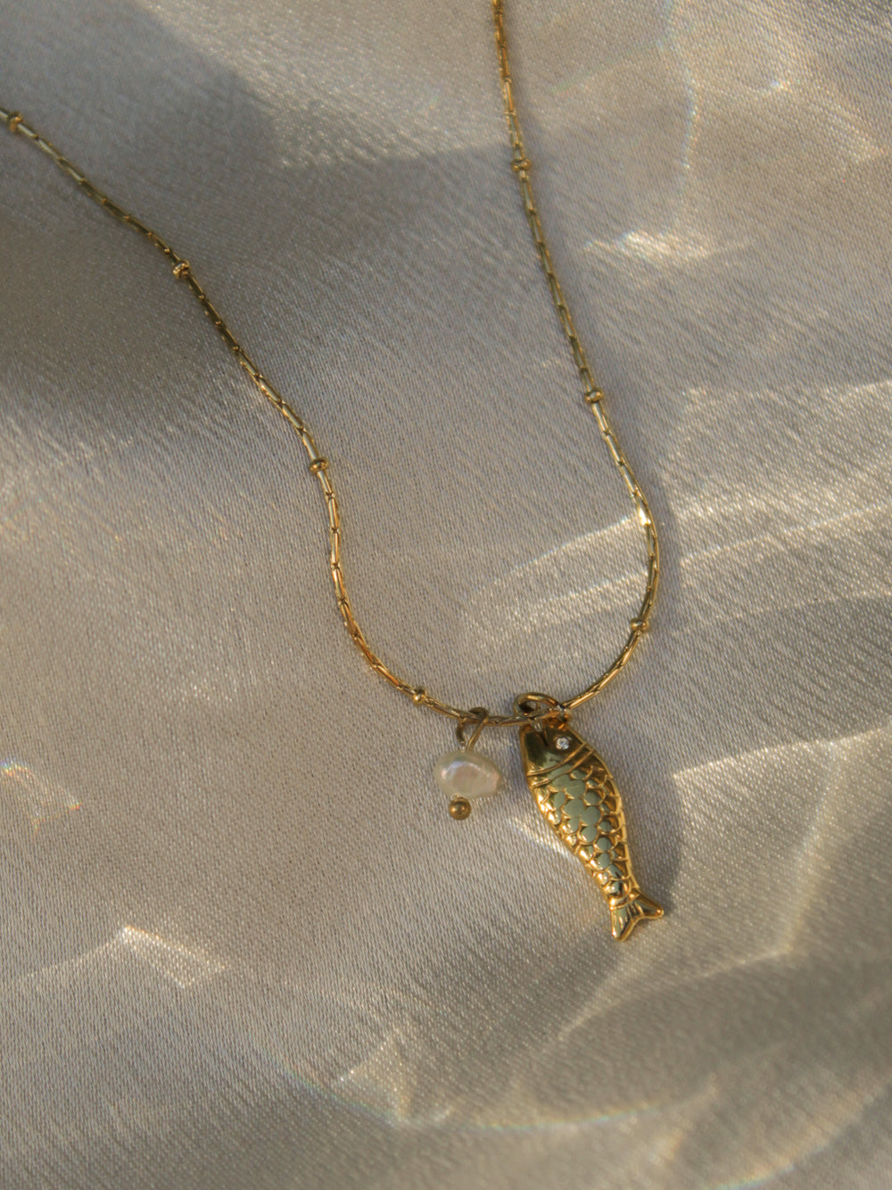 Dainty gold necklace with a fish and a pearl charm