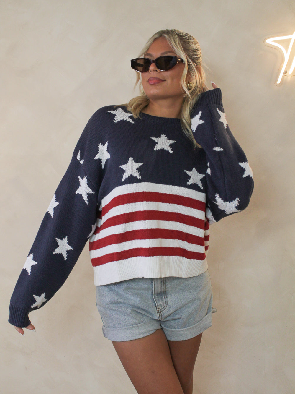 Woman wearing an american flag sweater paired with denim shorts and cat eye sunglasses