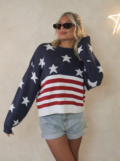 Woman wearing an american flag sweater paired with denim shorts and cat eye sunglasses