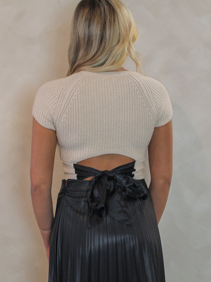 Woman wearing a cream short sleeve sweater with a bow tie detail in the back 