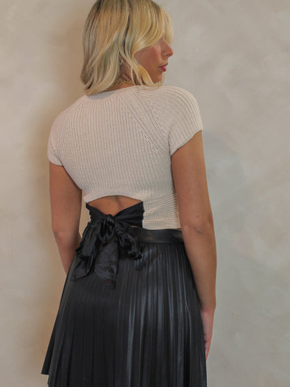 Woman wearing a cream sweater with a black satin bow detail on the back 