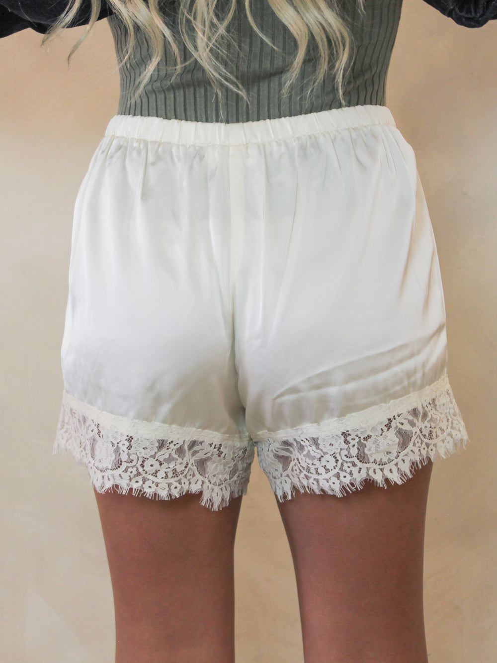Ivory satin shorts with a delicate lace hem, shown on a model from the back.