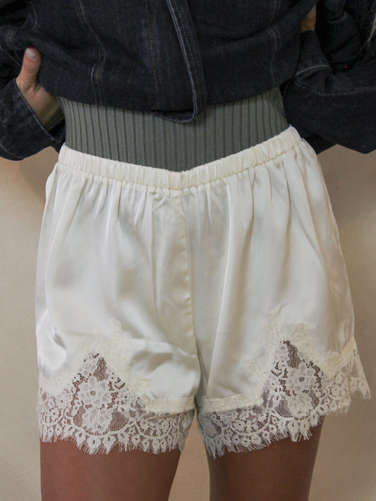 Ivory satin shorts with a floral lace hem.