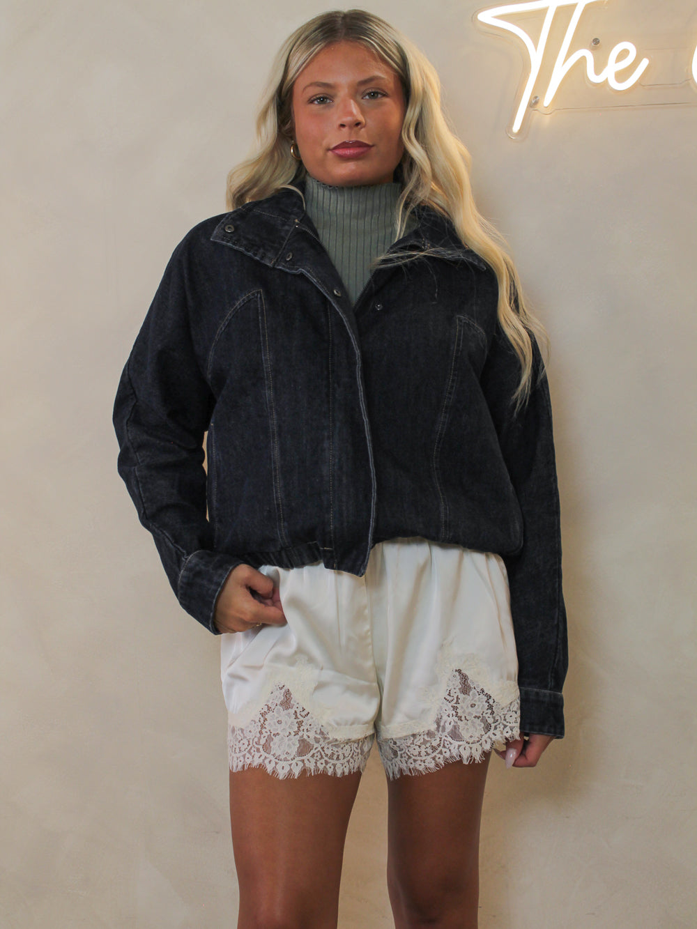 Model wearing a dark washed denim jacket styled with ivory shorts with lace trim.