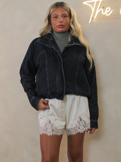 Model wearing a dark washed denim jacket styled with ivory shorts with lace trim.