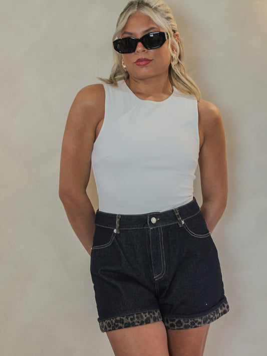 girl wearing dark wash denim shorts for women with a leopard print cuffed hem styled with a white bodysuit and black sunglasses outfit 