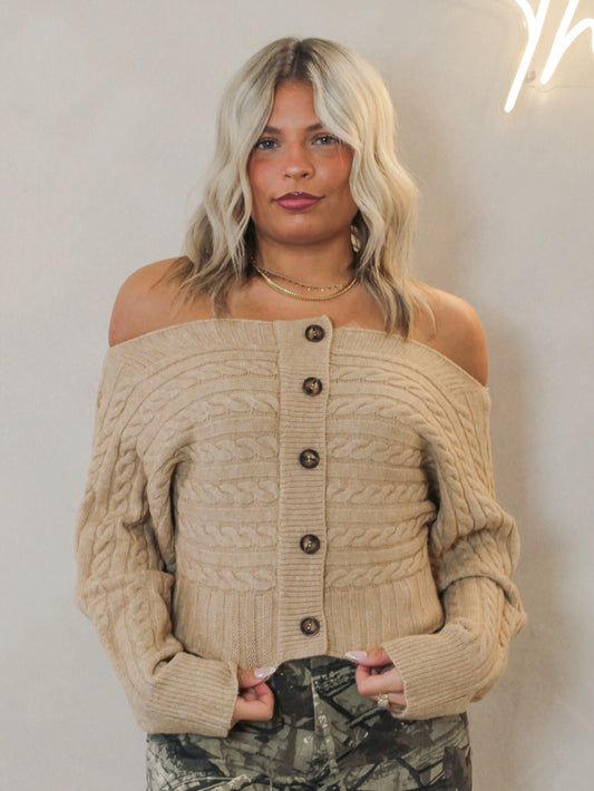 Woman wearing a beige off-shoulder cable knit sweater 
