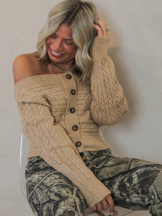 Woman wearing a beige cable knit, off the shoulder cardigan with camo pants 