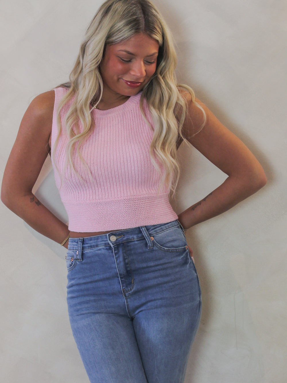 Model wearing a cropped, pink, sleeveless sweater top 