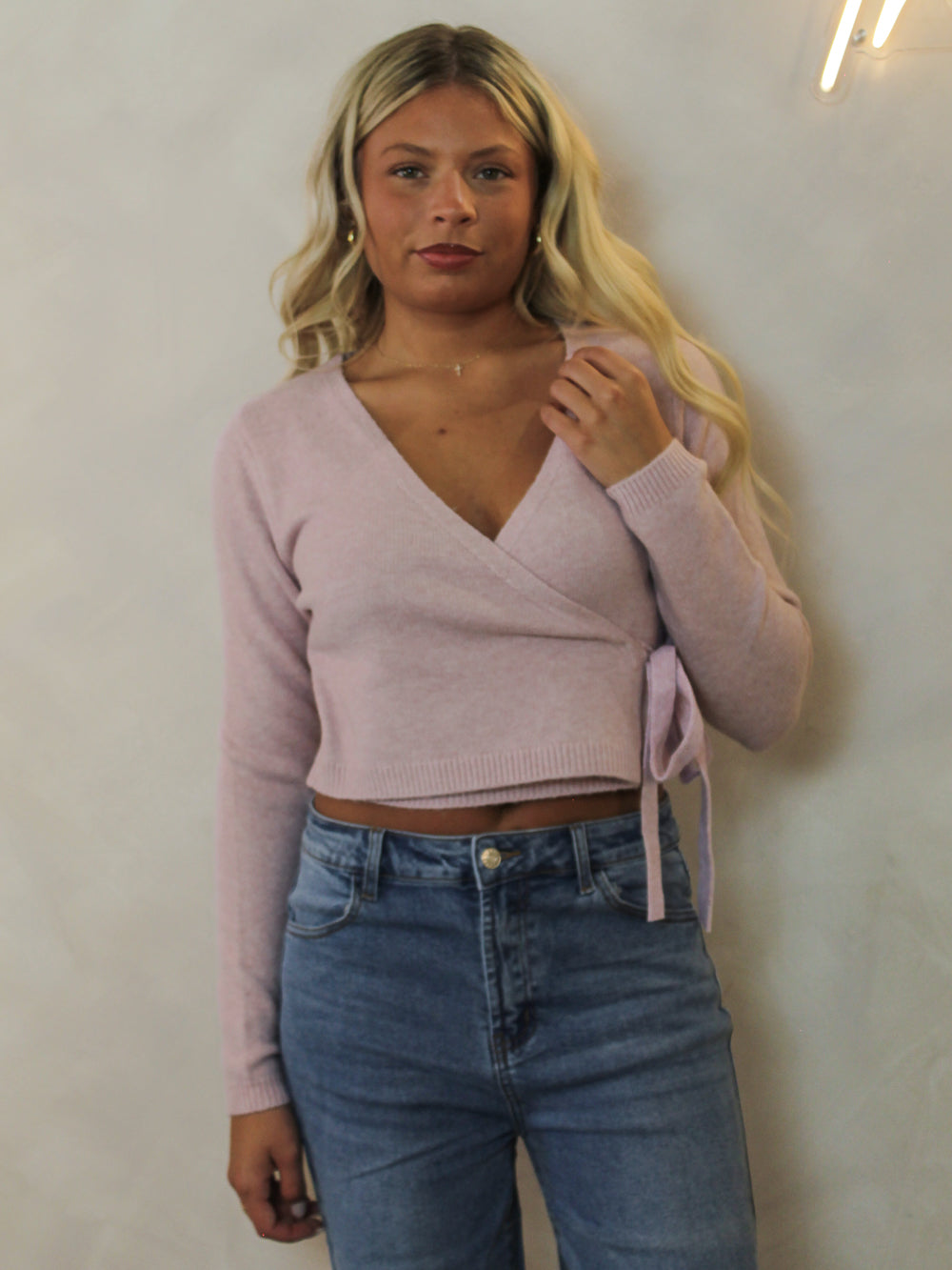 Model wearing a light pink, wrap style sweater styled with denim.