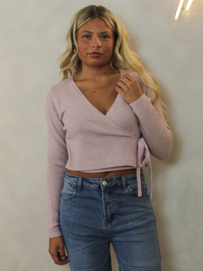 Model wearing a light pink, wrap style sweater styled with denim.