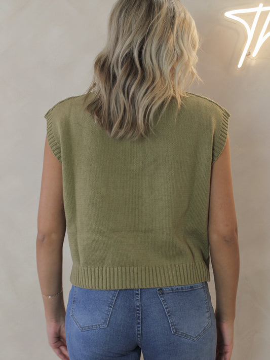 Woman wearing a sleeveless knit sweater in an olive color 
