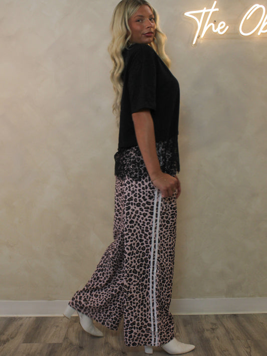 Model wearing a pair of leopard track style pants and a black t-shirt with a lace trim.