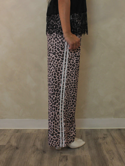 A person shown from the waist down wearing wide-leg leopard-print pants with white side stripes, a black lace top, and white shoes.