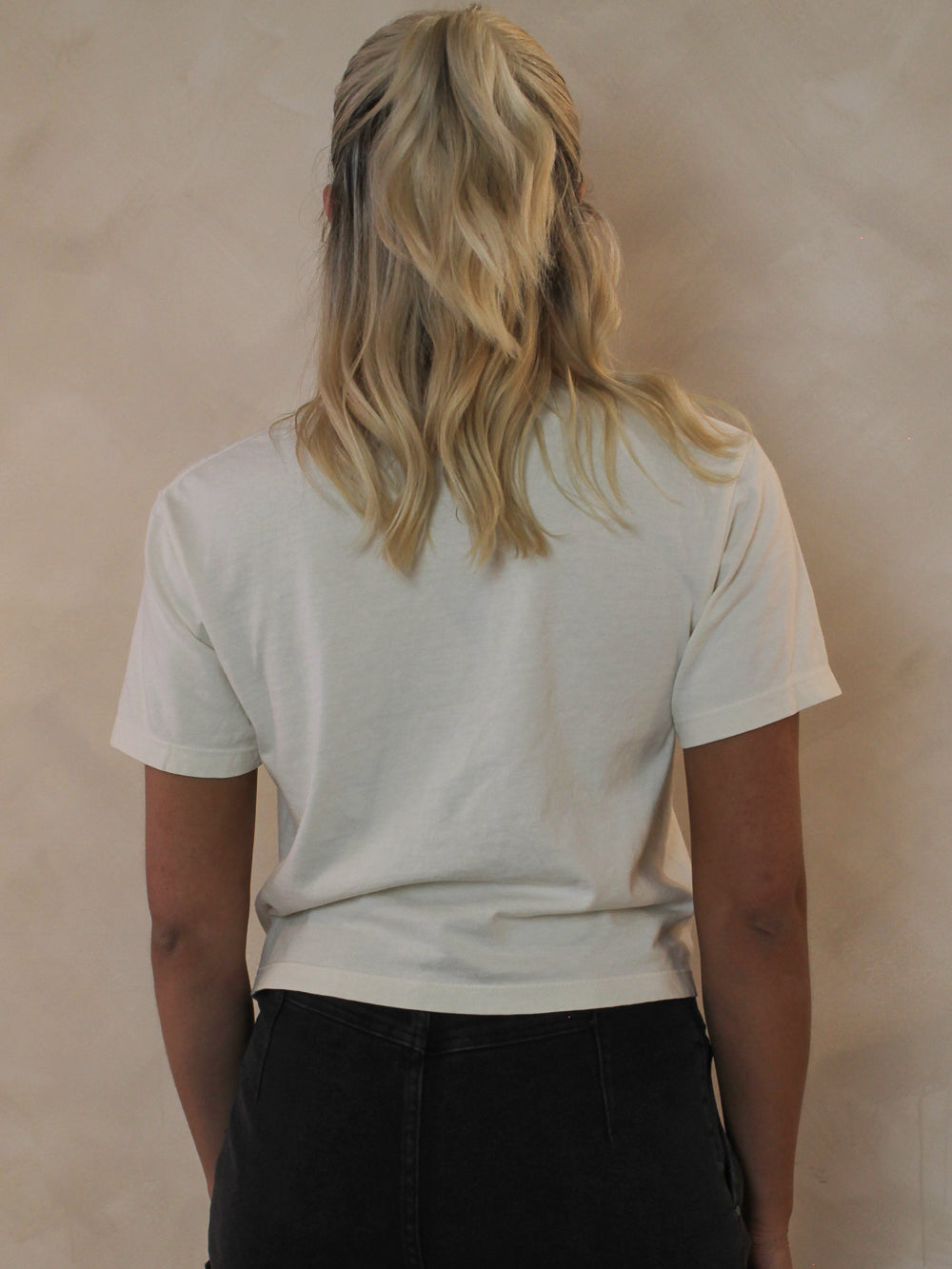 Woman wearing an off white cropped tee from the back