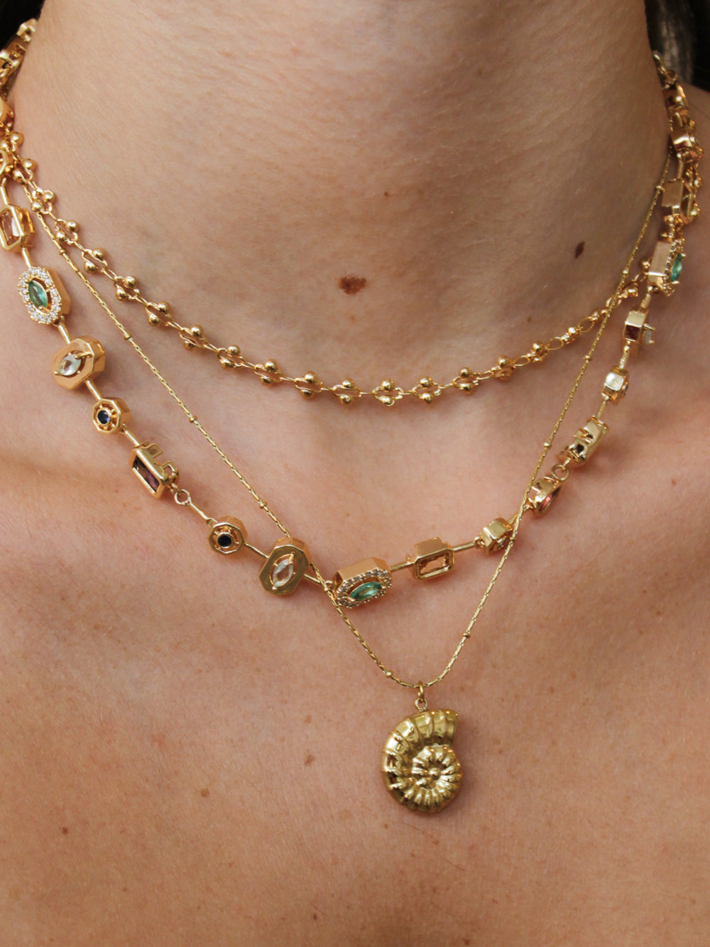 Gold necklace stack featuring a shell pendant necklace. 