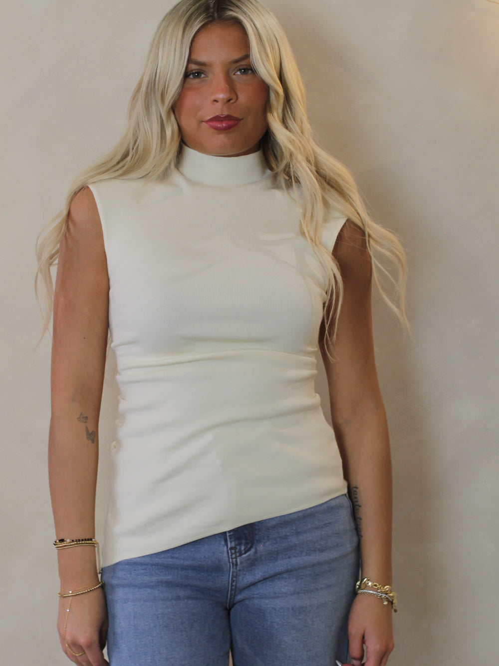 Woman wearing a white, mock neck sleeveless top and blue jeans