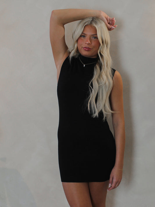 Model wearing a short black dress with cap sleeves and mock neck 