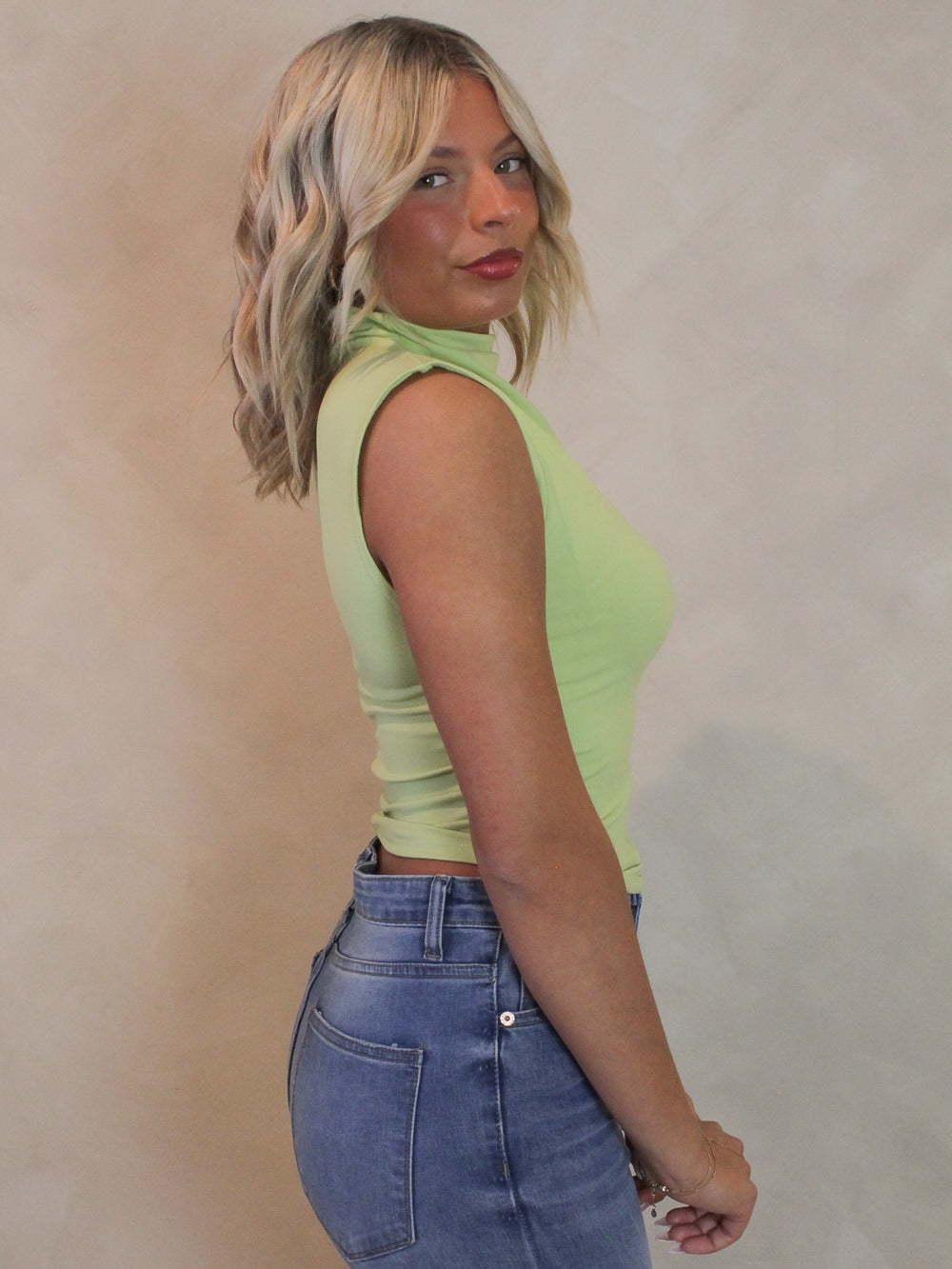 Woman wearing a sleeveless lime green top with ruched sides and mock nack