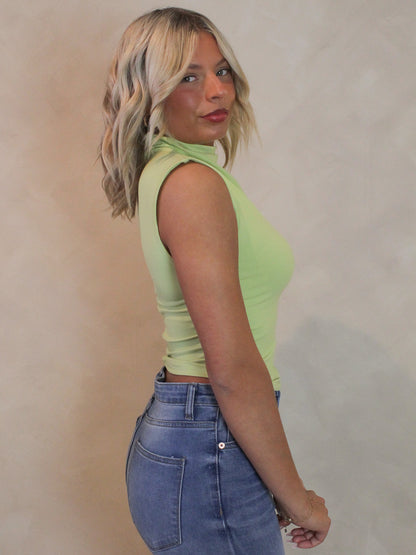 Woman wearing a sleeveless lime green top with ruched sides and mock nack