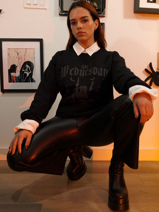 Woman wearing a black halloween crewneck sweatshirt that says On Wednesdays We Wear Black in black gothic font