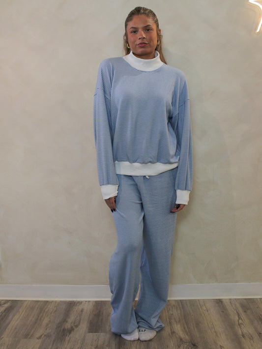 A woman wearing a blue and white striped lounge set, including a mock neck and wide leg pants.